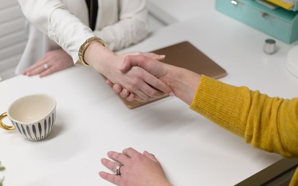 Two people shaking hands across a desk at the start of a project