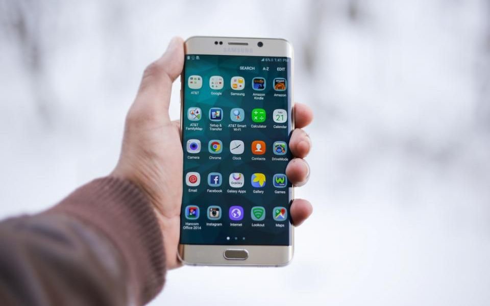 A hand holding a smartphone with a home screen full of apps