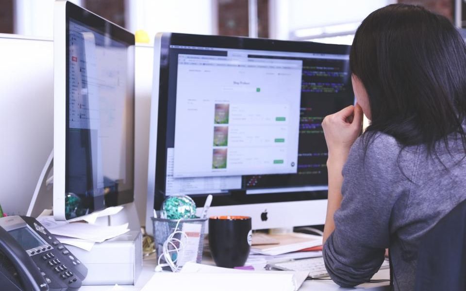 A support engineer working at a desk with two monitors and a phone